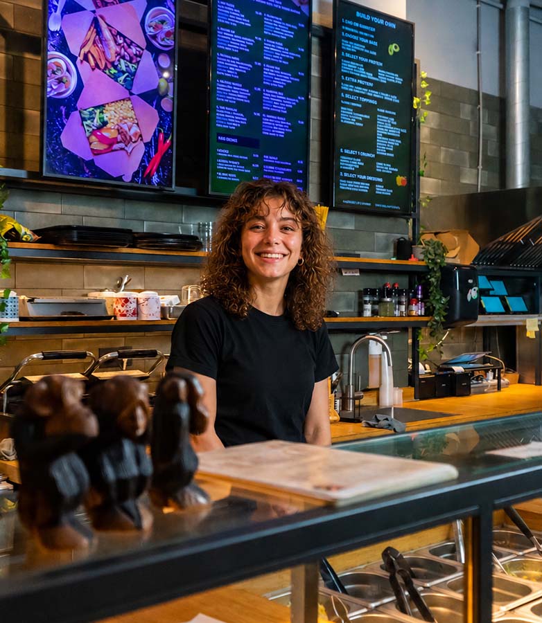 Membre de l'équipe de Grlla Kitchen derrière le comptoir avec les écrans de menu Onesix